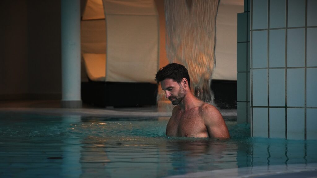 Mann unter Wasserfall im Pool
