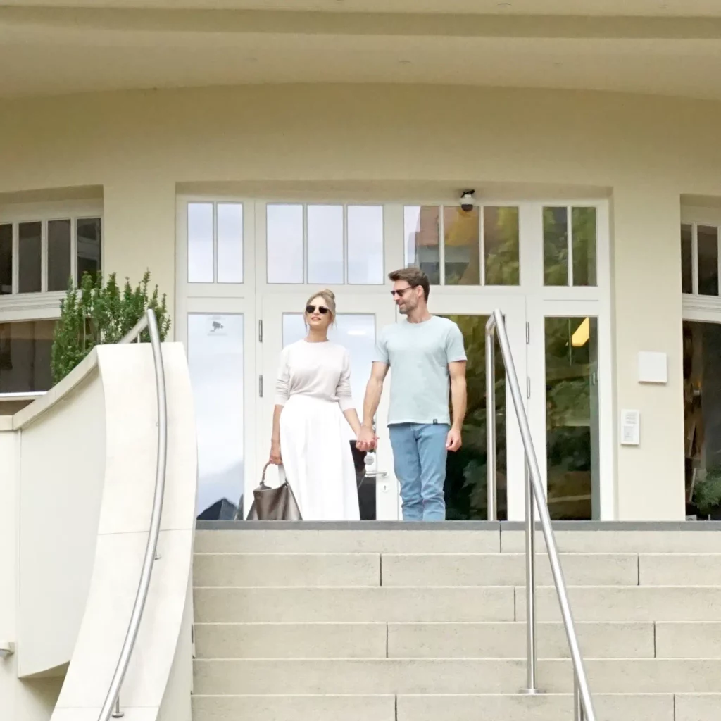 Eingang des Hotels mit Pärchen auf Treppe vor heller Fassade