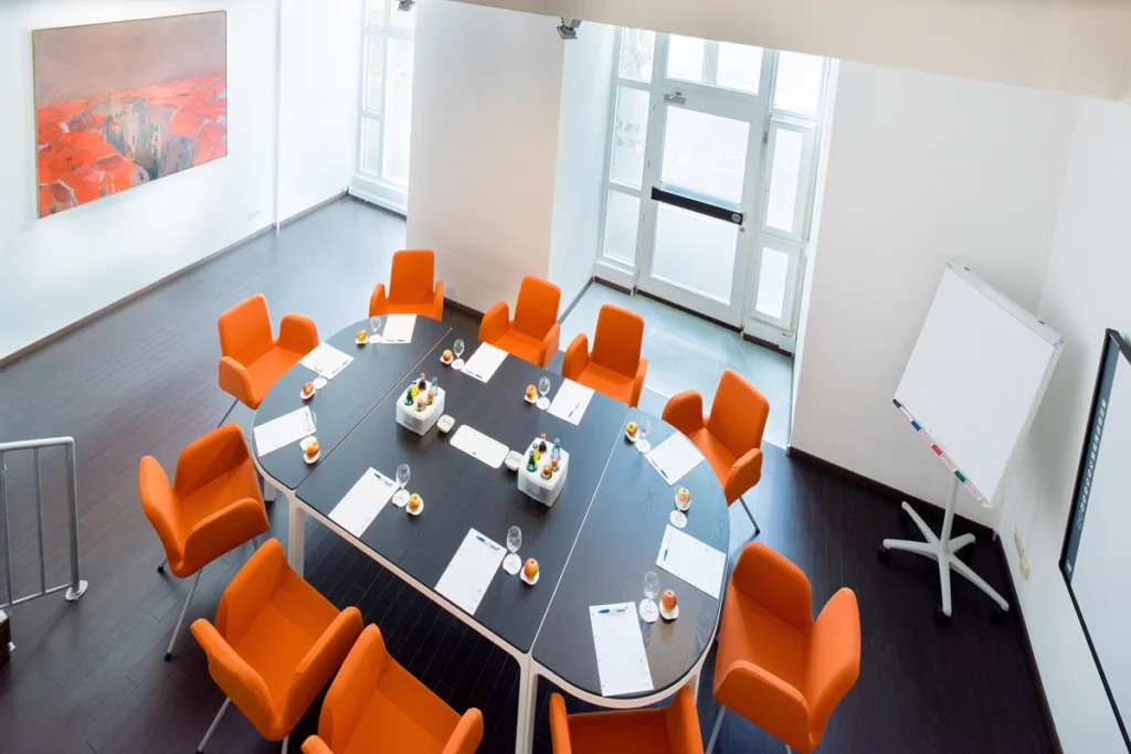 Großer Tisch im Tagungsraum mit orangenen Stühlen